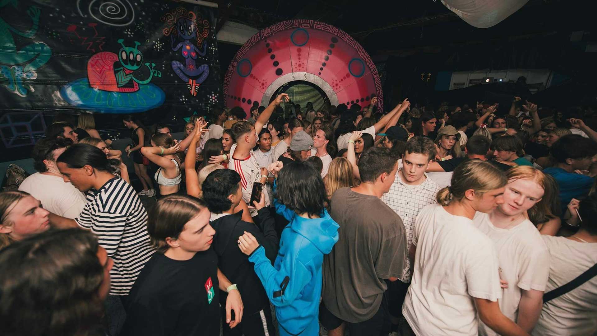 A large UFO themed warehouse full of ravers enjoying ambient electronic music performed by DJs.